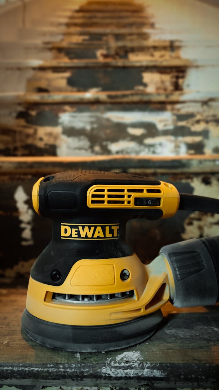 A DeWalt electric sander is prominently displayed on a worn staircase with peeling paint.